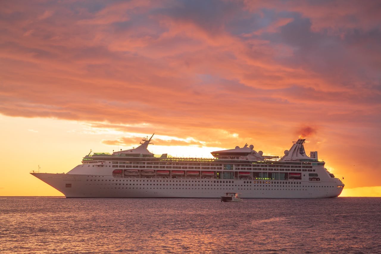 A majestic cruise ship sails across the Caribbean Sea at sunset in Grenada, showcasing a vibrant orange sky.